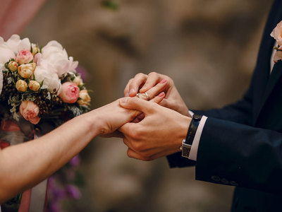 close up of man sliding wedding ring on woman's finger