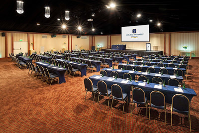 large conference room with projection screen and rows of tables and chairs 